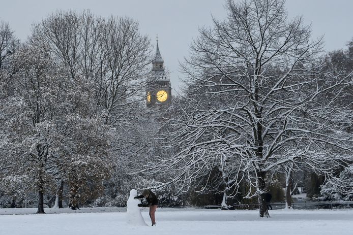 A London resident builds a snowman in a park against the backdrop of Big Ben.